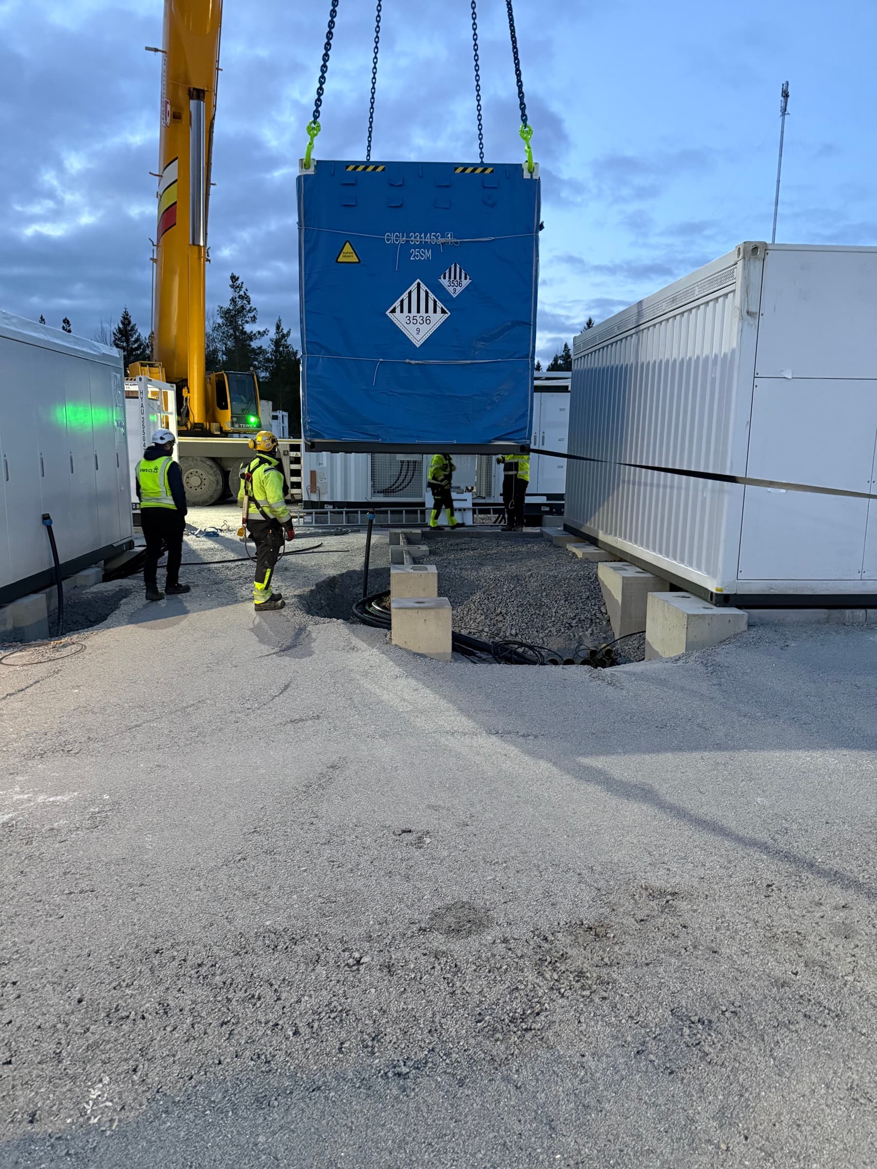 Contenedor de batería elevado por grúa con trabajadores supervisando